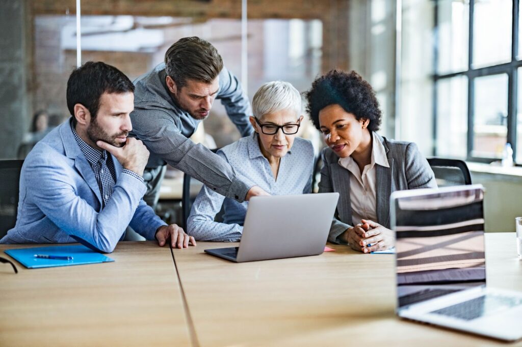 Four business professionals working together around a laptop.